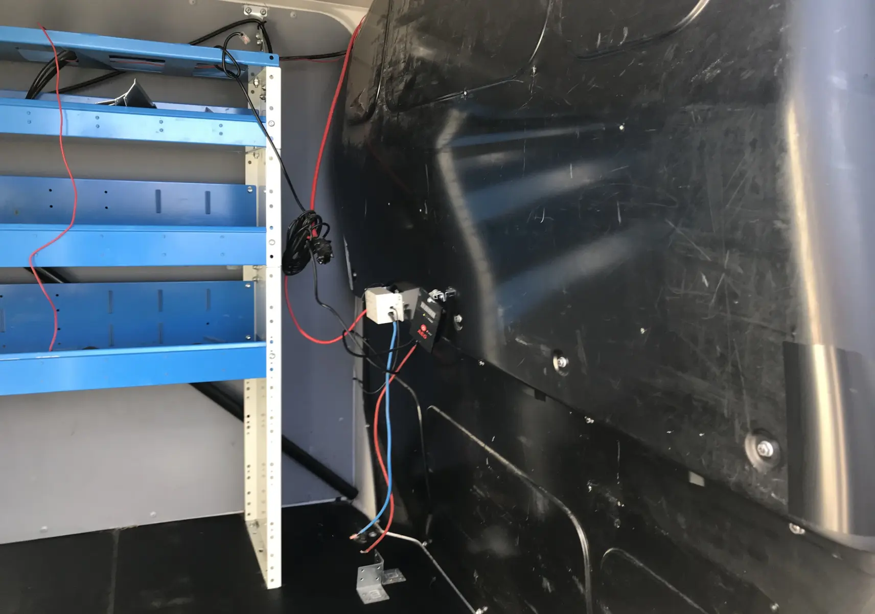 Vue intérieure arrière droite du Volkswagen Transporter T6 blanc, montrant des étagères bleues et une cloison noire.