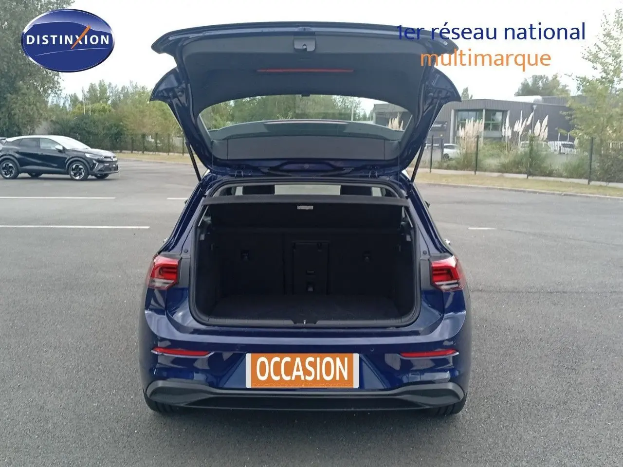 Vue arrière d'une Volkswagen Golf VIII bleu Atlantique métal avec coffre ouvert sur un parking extérieur.