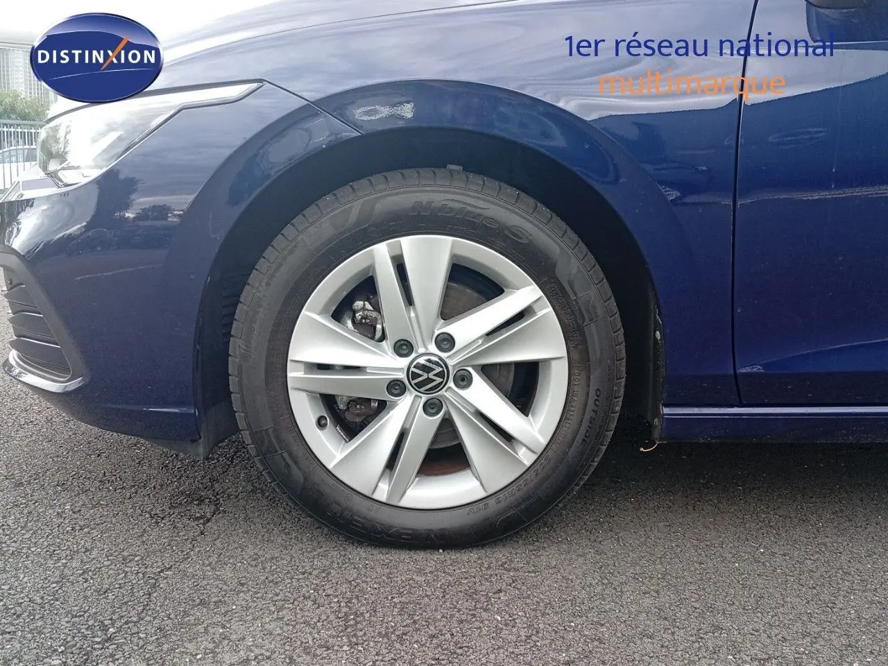 Gros plan sur la roue avant gauche d'une Volkswagen Golf VIII bleu Atlantique métal avec jante alliage 16 pouces.