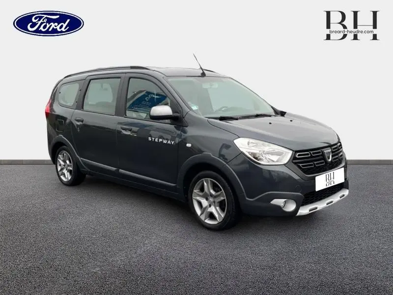 Dacia Lodgy Stepway gris Comète vue 3/4 avant droit avec barres de toit et jantes alliage visibles.