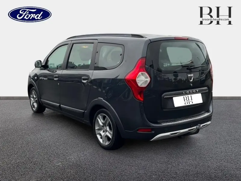 Vue 3/4 arrière droite d'un Dacia Lodgy Stepway gris Comète avec barres de toit et attelage visible