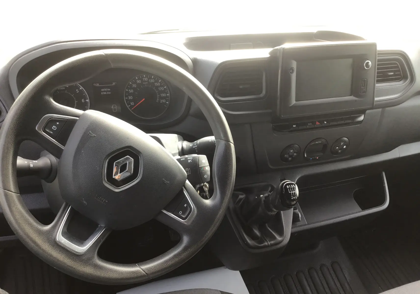 Vue intérieure du poste de conduite du Renault Master blanc, avec volant, tableau de bord et levier de vitesses manuel visibles.