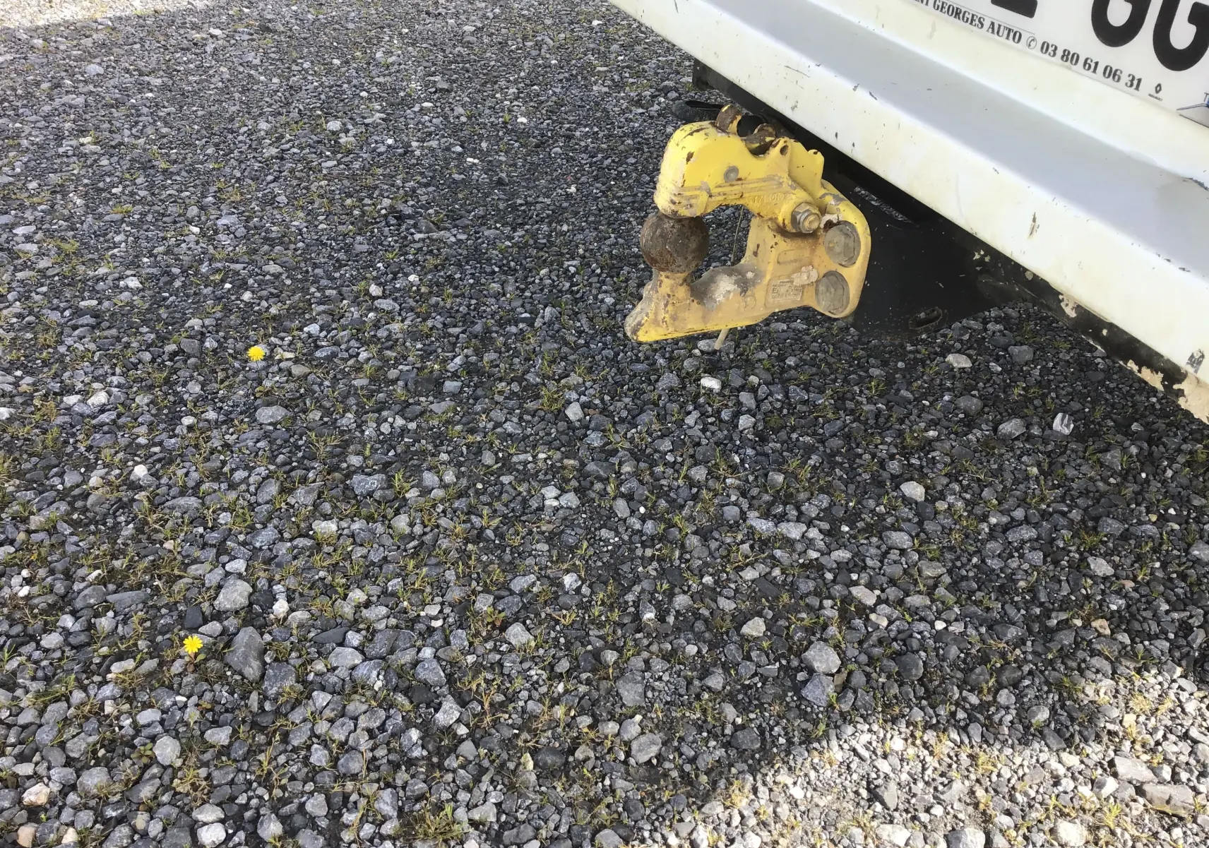 Vue rapprochée de l'arrière blanc d'un Renault Master avec attelage jaune sur un sol gravillonné.