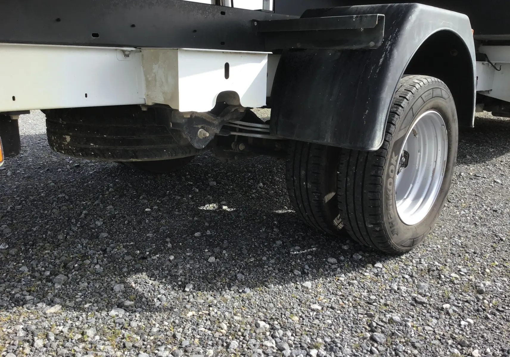 Gros plan sur l'essieu arrière droit blanc du Renault Master Châssis Cabine avec benne et coffre, roues jumelées visibles.