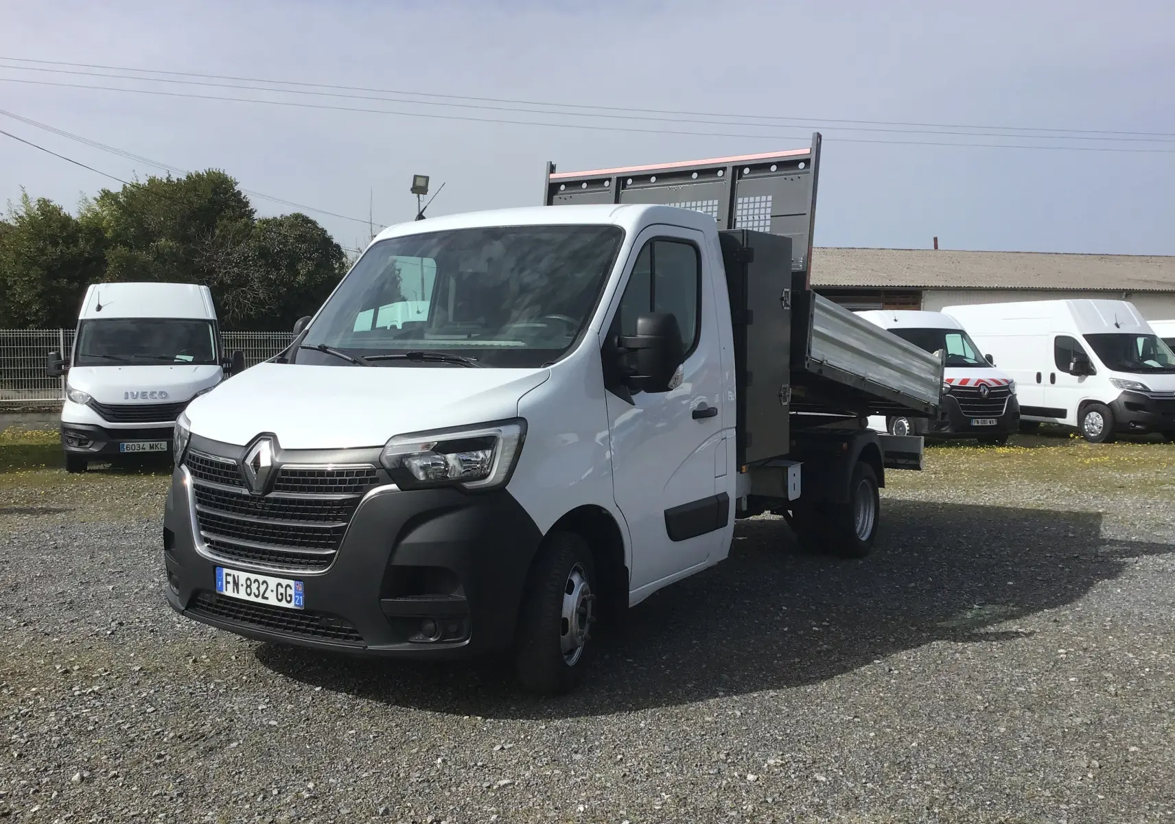 Renault Master blanc en 3/4 avant droit, benne relevable avec coffre latéral et grille de protection des feux.