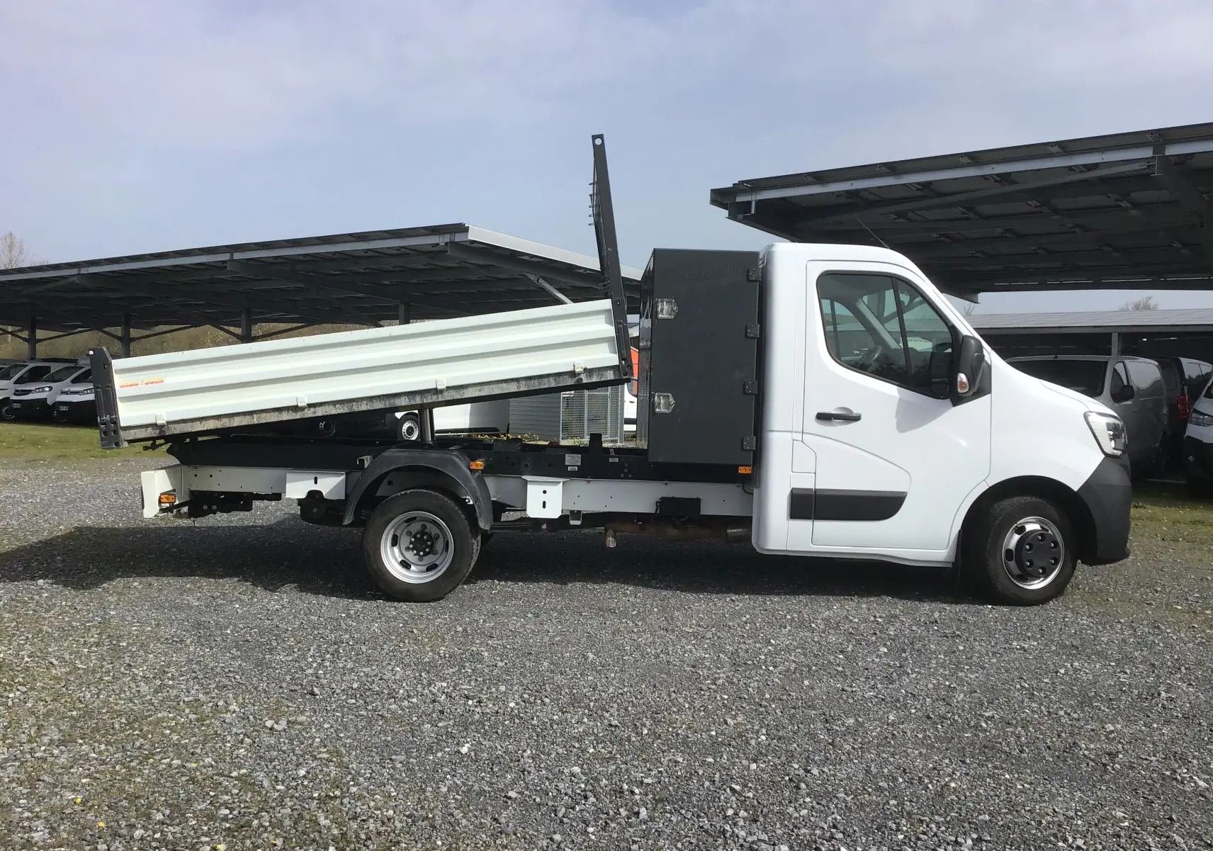 Vue latérale droite d’un Renault Master blanc avec benne basculante relevée et coffre noir derrière la cabine.