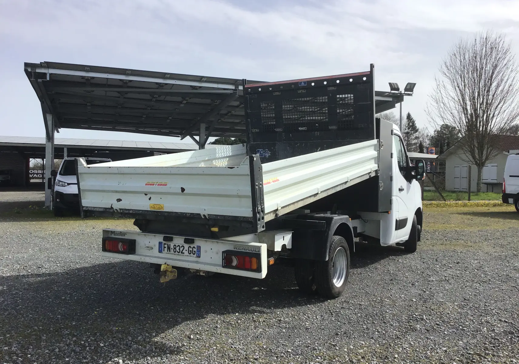 Renault Master Châssis cabine blanc vu 3/4 arrière droit, avec benne relevée et grille de protection noire.