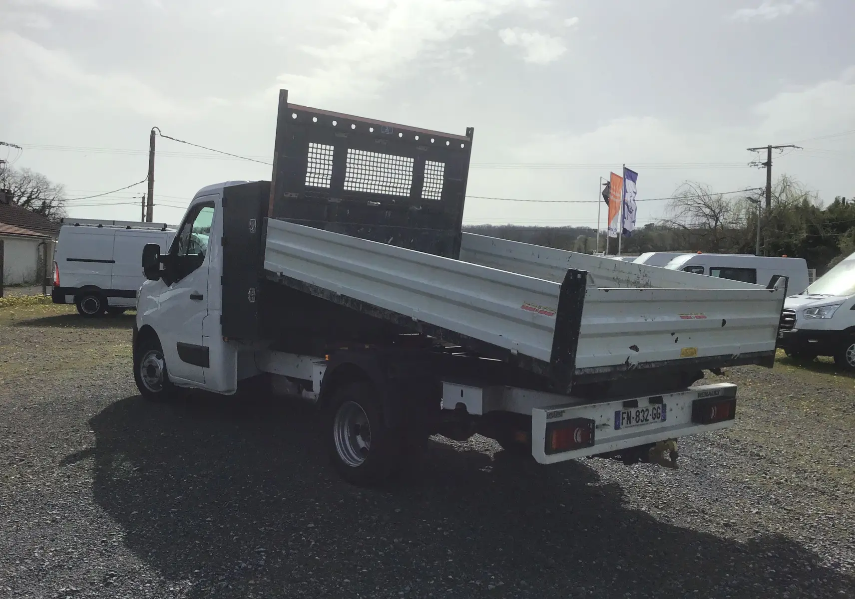 Vue 3/4 arrière droite d’un Renault Master blanc avec benne relevée et grille de protection noire sur cabine.