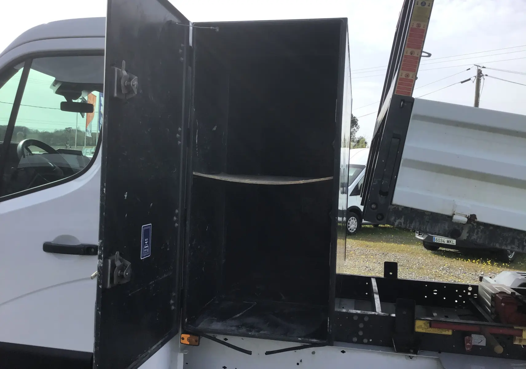 Vue latérale gauche d’un Renault Master blanc avec coffre ouvert et benne relevée, montrant la structure et le rangement arrière.