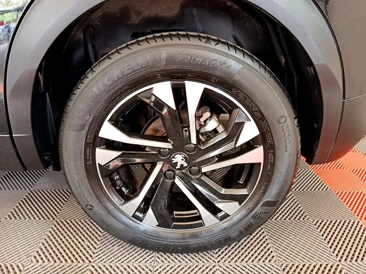 Gros plan sur la roue avant droite noire d’un Peugeot 2008 2021 avec jante alliage bicolore et pneu Michelin.