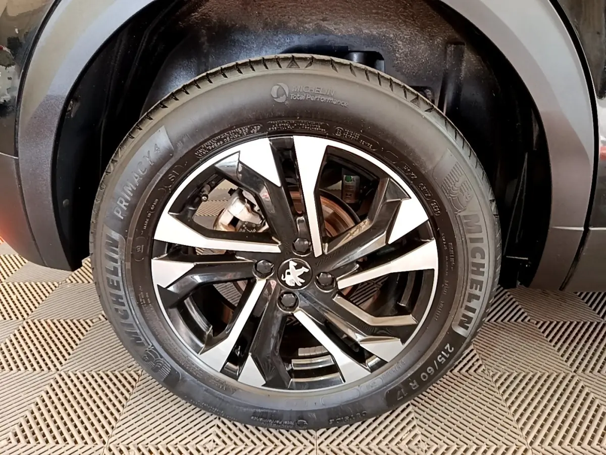 Gros plan sur la roue avant droite noire et argentée d’un Peugeot 2008 noir, avec logo lion au centre.