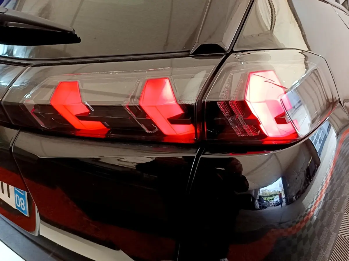 Gros plan sur le feu arrière droit rouge d’un Peugeot 2008 noir, reflétant l’environnement intérieur.