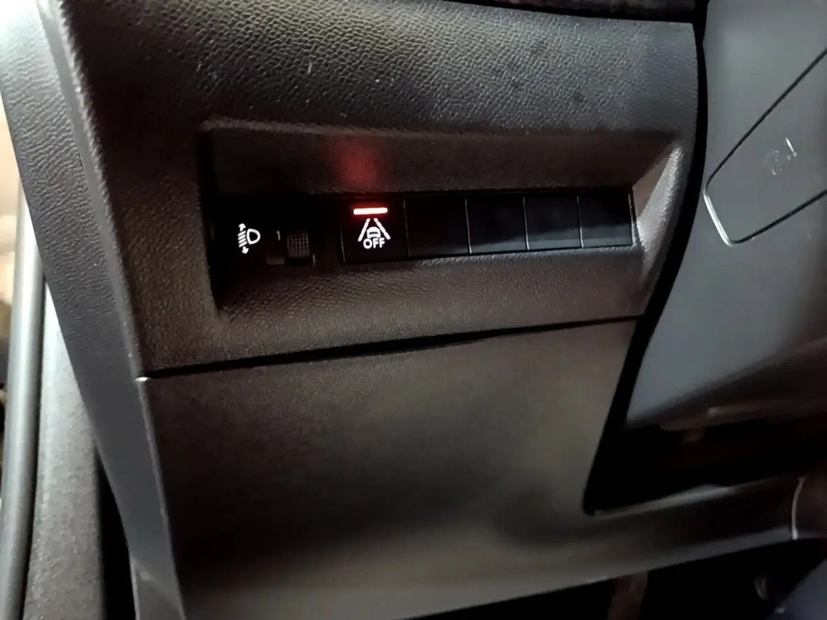 Détail intérieur du tableau de bord côté conducteur du Peugeot 2008 noir, bouton d'assistance à la conduite désactivée.