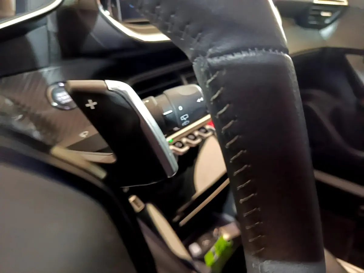Gros plan sur le volant cuir noir et la palette de changement de vitesse + du Peugeot 2008 Diesel 2021, intérieur moderne.