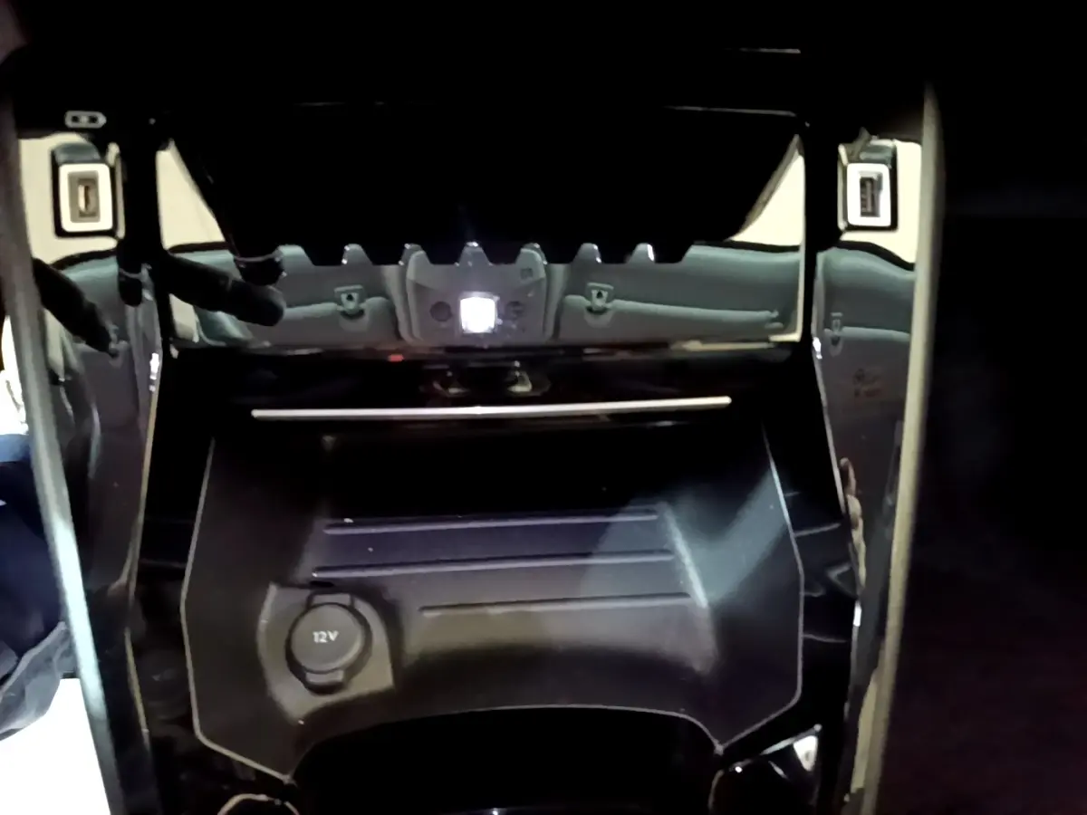 Gros plan sur la console centrale noire du Peugeot 2008 2021 avec prise 12V et finition brillante autour.