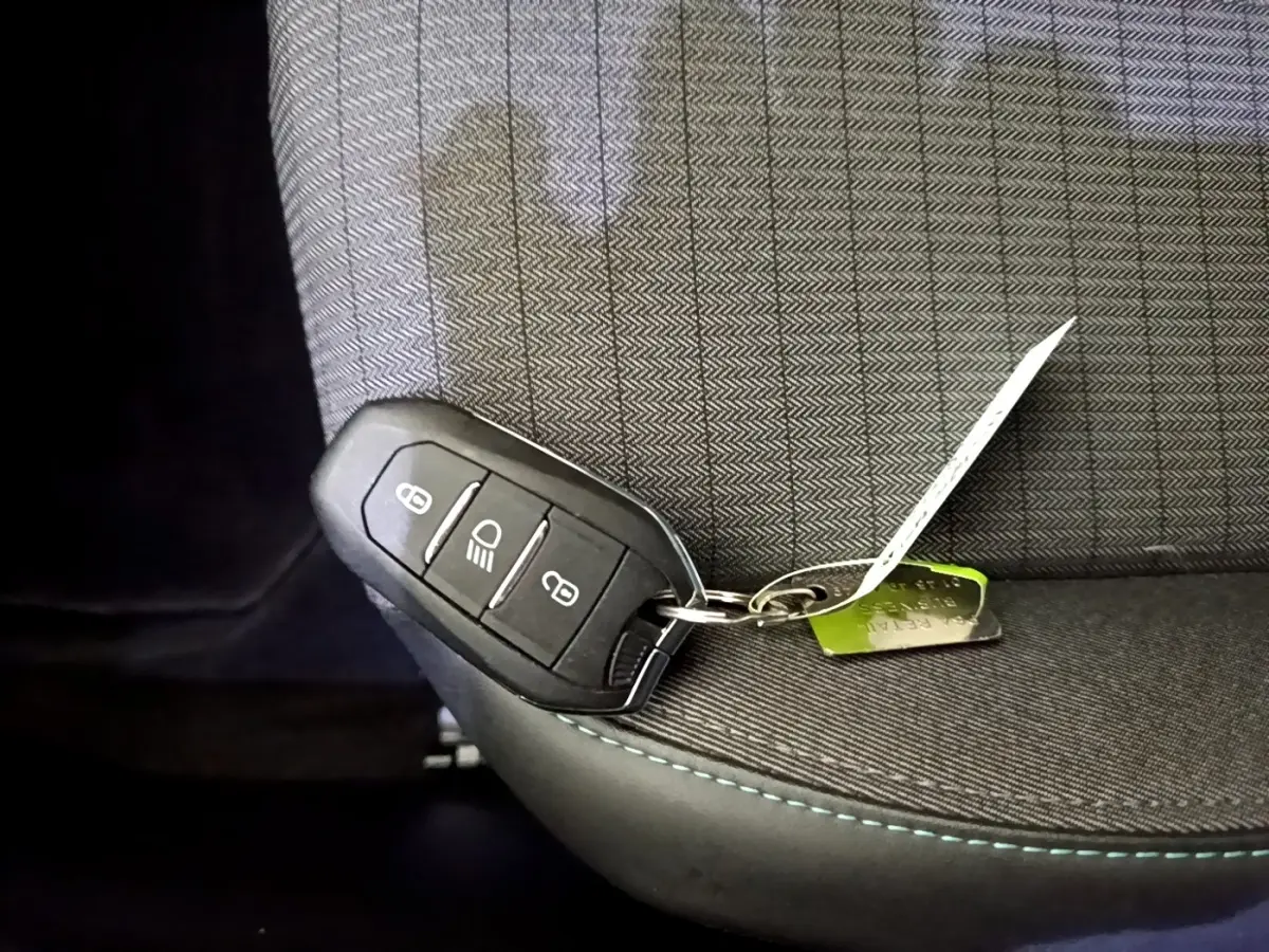 Clé de contact noire posée sur un siège tissu gris à surpiqûres bleues dans l'habitacle d'une Peugeot 2008 noire.