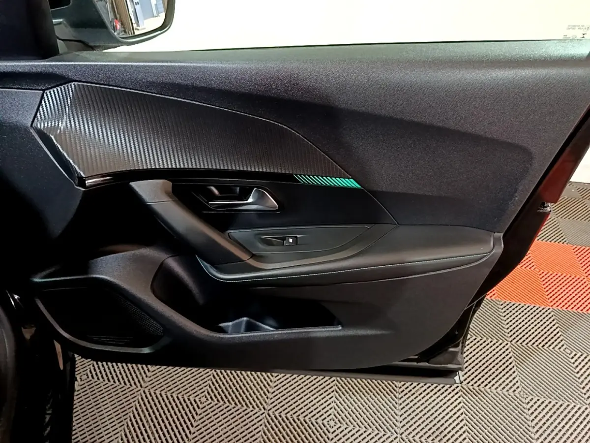 Vue intérieure du panneau de porte avant gauche noir du Peugeot 2008 2021 avec insert effet carbone et bouton de lève-vitre.