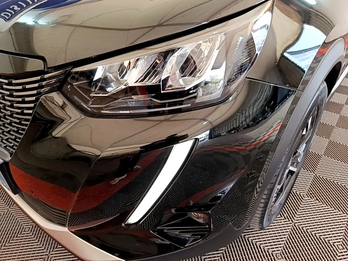 Gros plan sur l'avant droit noir brillant du Peugeot 2008 2021, mettant en valeur le phare LED et la calandre distinctive.