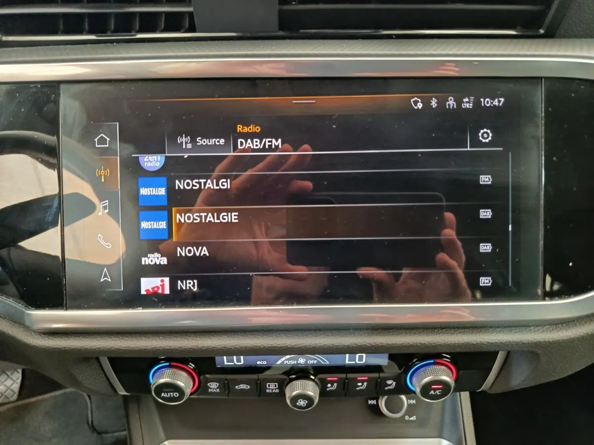 Écran tactile central de l’Audi Q3 Sportback 35 TDI 2023 affichant les stations radio DAB/FM, avec commandes climatisation en dessous.