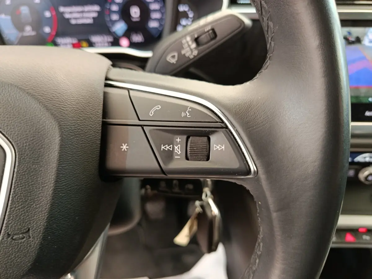 Gros plan sur le volant cuir noir de l'Audi Q3 Sportback 35 TDI, avec commandes multifonctions et tableau de bord numérique flou.