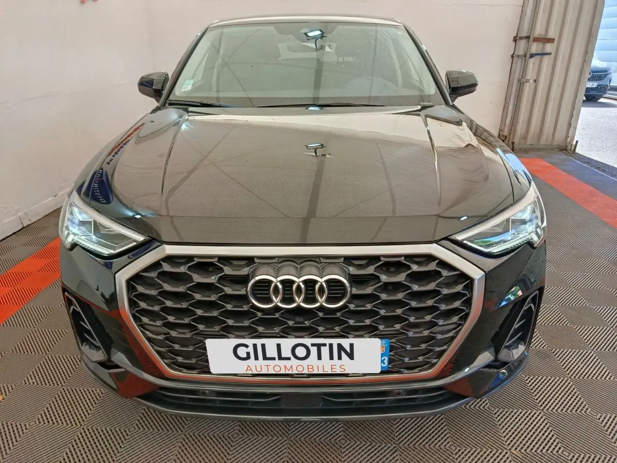 Vue avant d’un Audi Q3 Sportback noir 2023 avec calandre hexagonale et phares LED allumés dans un garage.