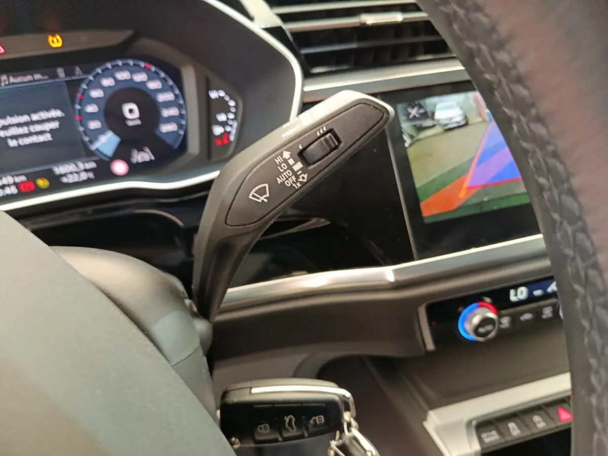 Vue intérieure rapprochée du volant et du commodo d’essuie-glace d’un Audi Q3 Sportback noir avec affichage numérique et écran multimédia.