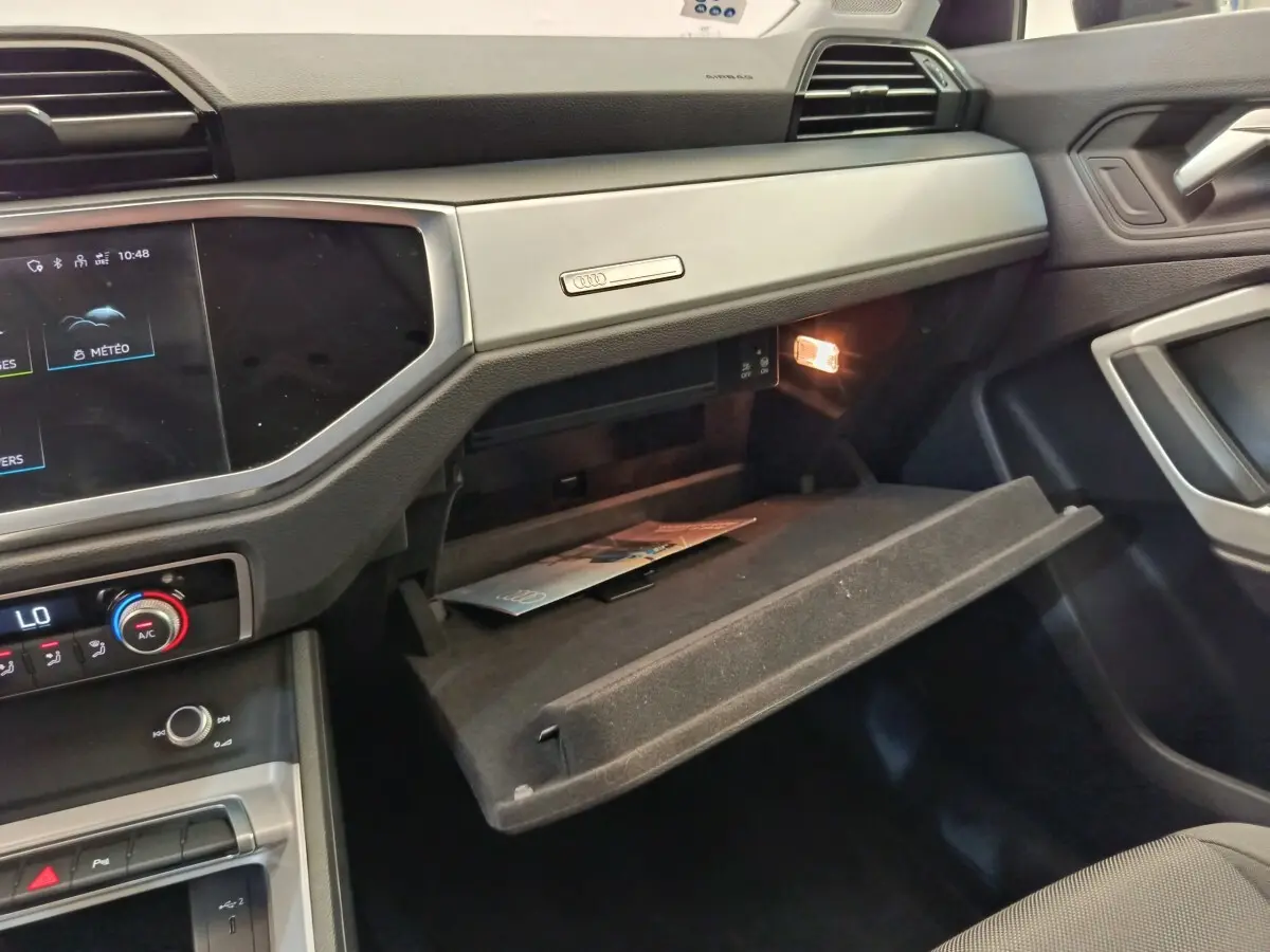 Intérieur de l'Audi Q3 Sportback 35 TDI 2023, vue côté passager avec boîte à gants ouverte et éclairage intérieur.