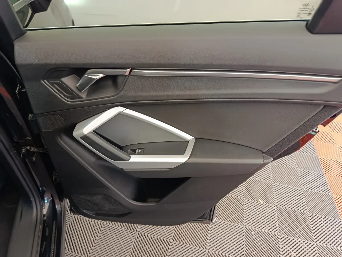 Vue rapprochée de la porte avant gauche noire de l’Audi Q3 Sportback 35 TDI avec poignée argentée et garniture intérieure noire.
