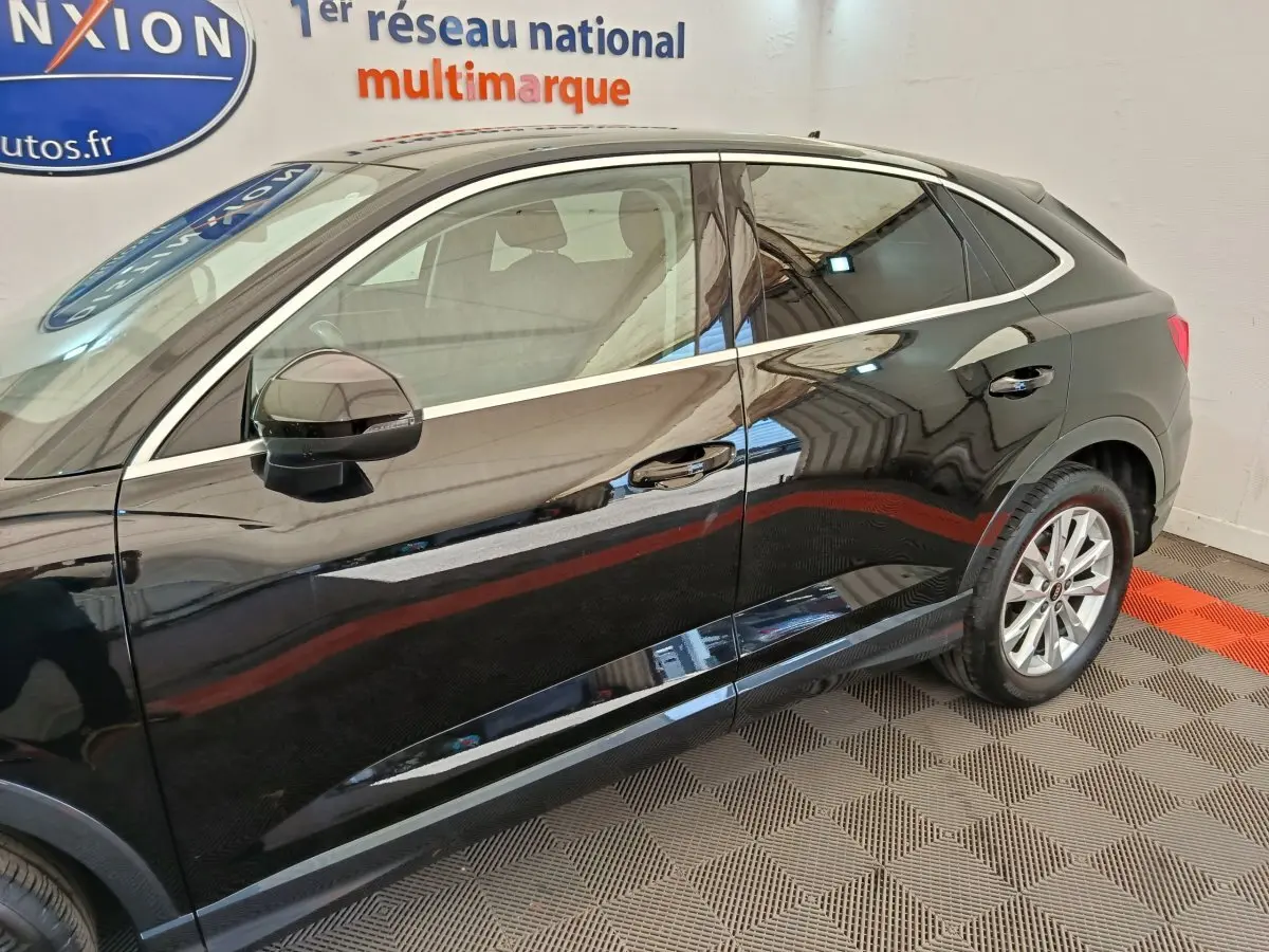 Vue de profil côté gauche d'un Audi Q3 Sportback noir brillant dans un showroom intérieur.