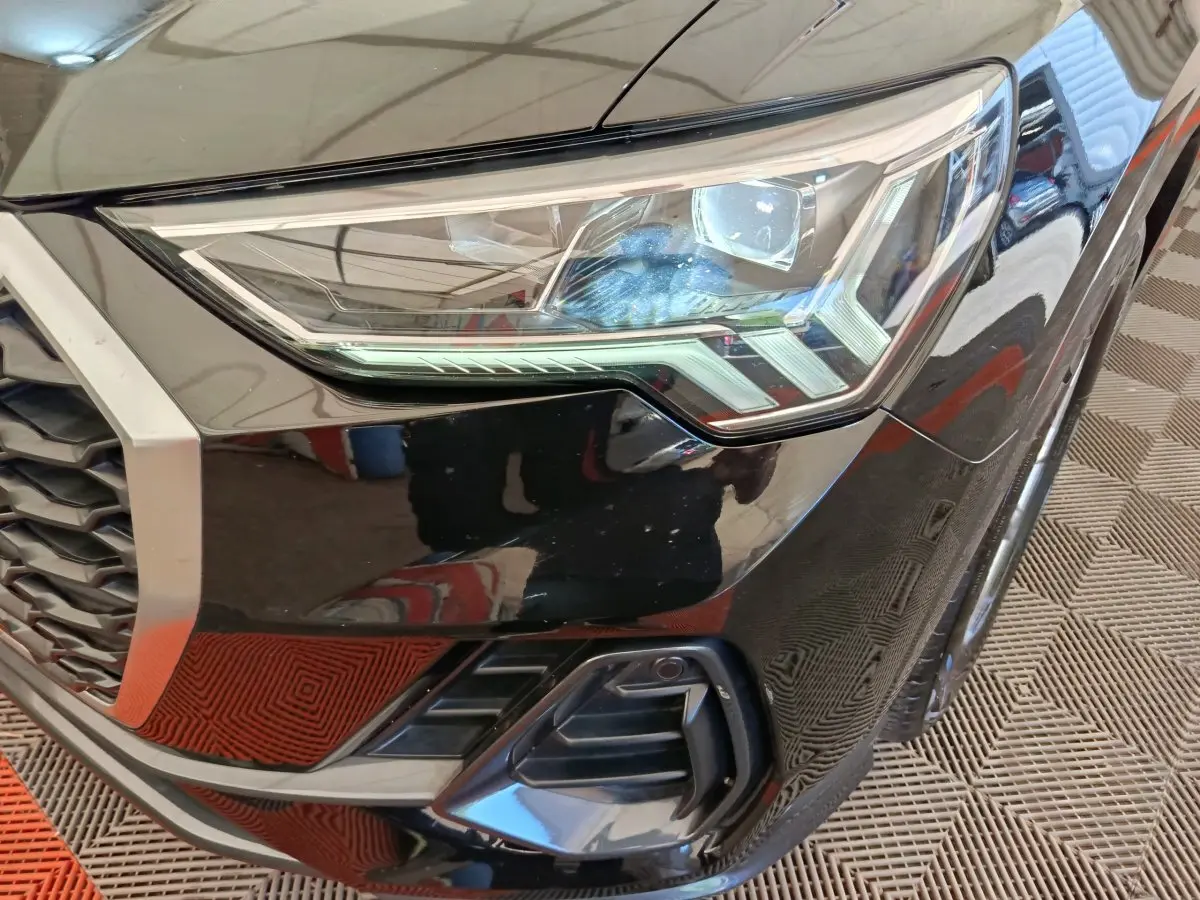 Gros plan sur le phare avant droit noir brillant de l'Audi Q3 Sportback 35 TDI 2023 avec calandre hexagonale.