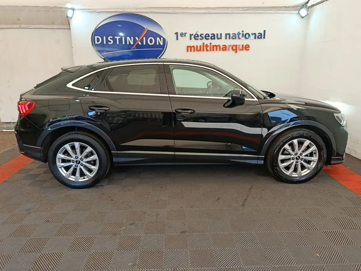 Vue latérale droite d'un Audi Q3 Sportback noir 2023, avec jantes alliage et lignes épurées sous un éclairage intérieur.