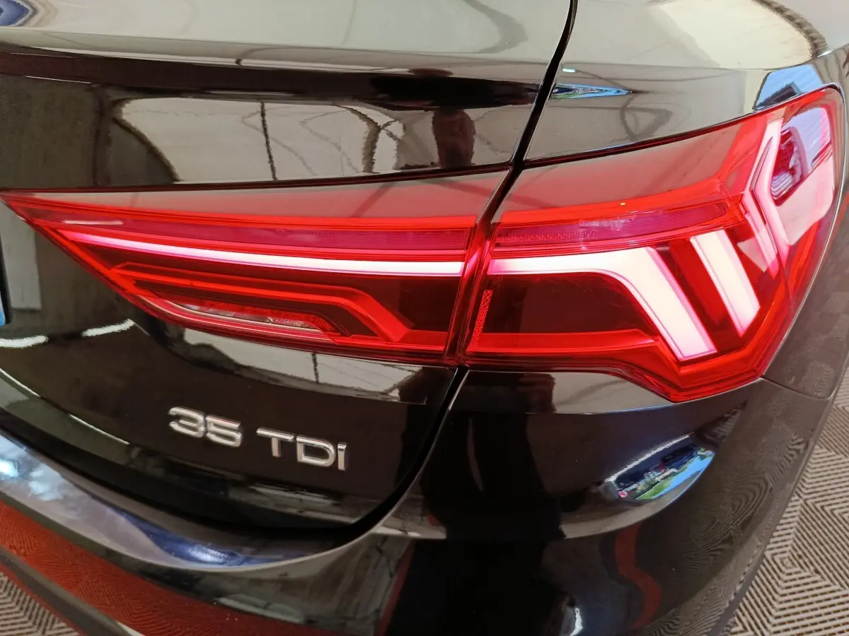 Gros plan sur le feu arrière droit rouge et le logo 35 TDI d’un Audi Q3 Sportback noir 2023.