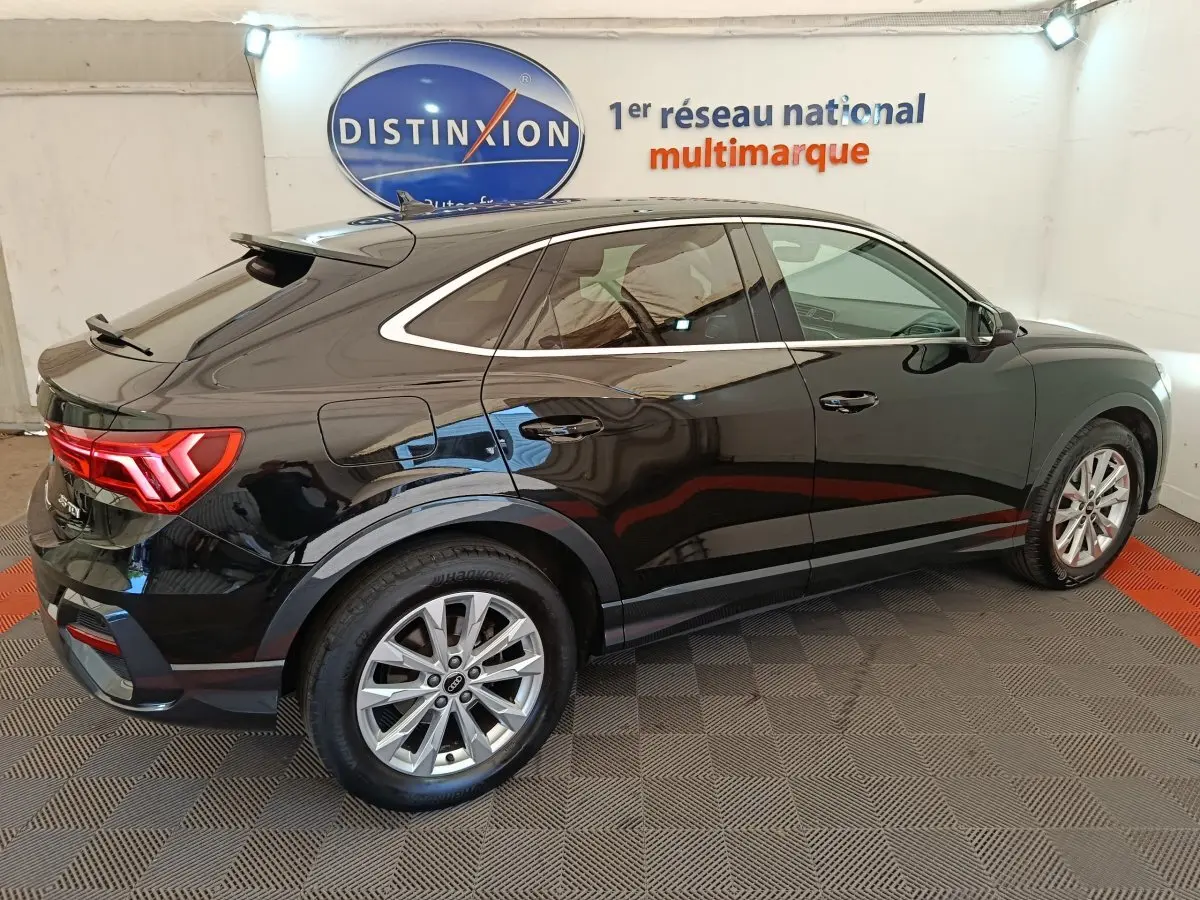 Audi Q3 Sportback noir vue 3/4 arrière droit, avec feux LED et jantes alliage visibles en intérieur showroom.