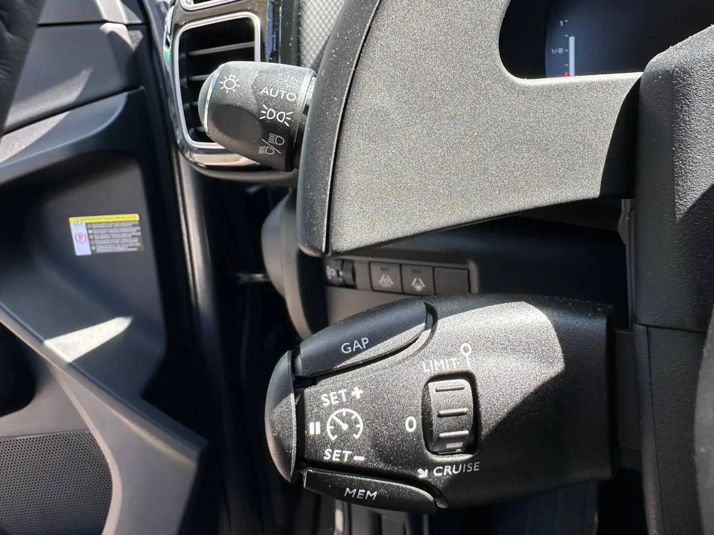 Gros plan sur la commande de régulateur de vitesse à gauche du volant dans l’habitacle noir du Citroën C5 Aircross gris Platinium.