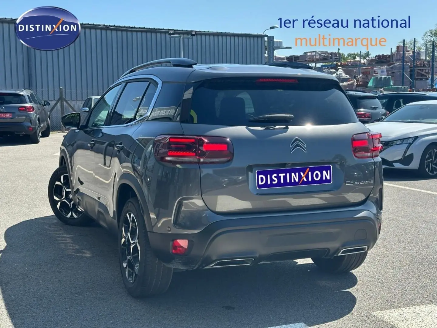 Vue 3/4 arrière droite d'un Citroën C5 Aircross gris Platinium avec barres de toit et feux arrière LED allumés.