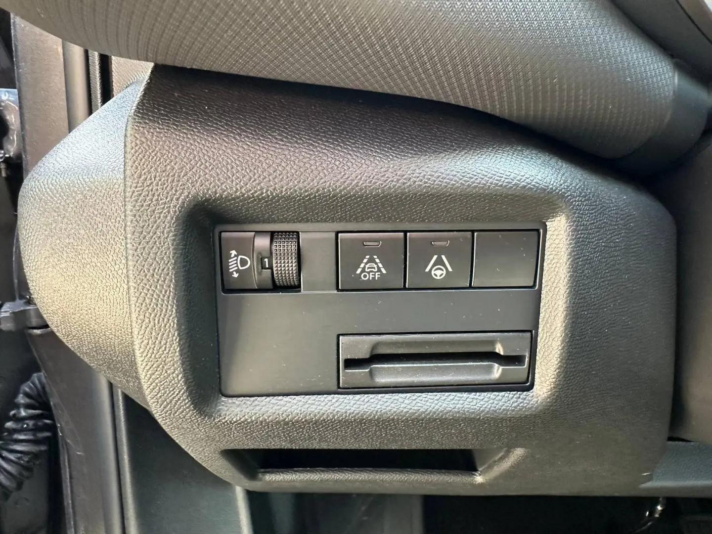 Vue rapprochée des commandes de réglage des phares et d'assistance à la conduite sur le côté gauche du tableau de bord gris du Citroën C5 Aircross.