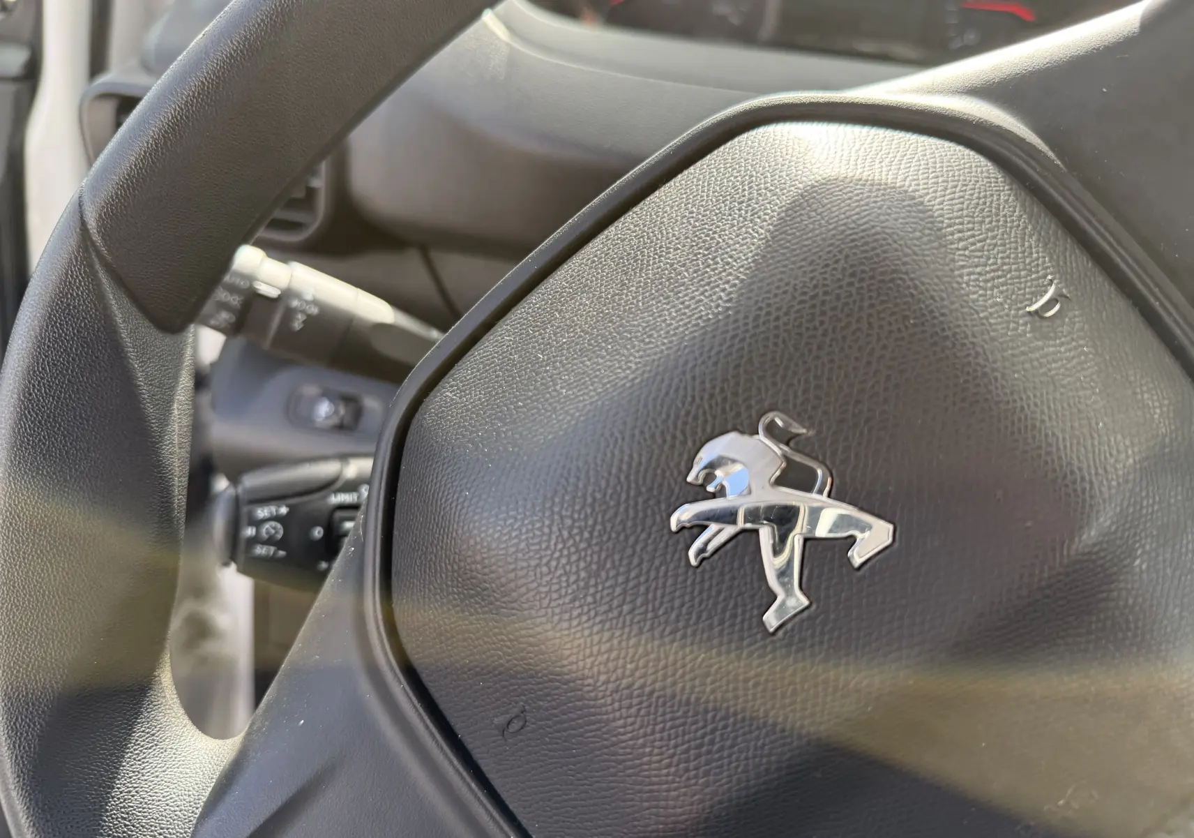 Gros plan sur le volant noir avec logo Peugeot du Partner blanc 2021, mettant en valeur les commandes au volant.