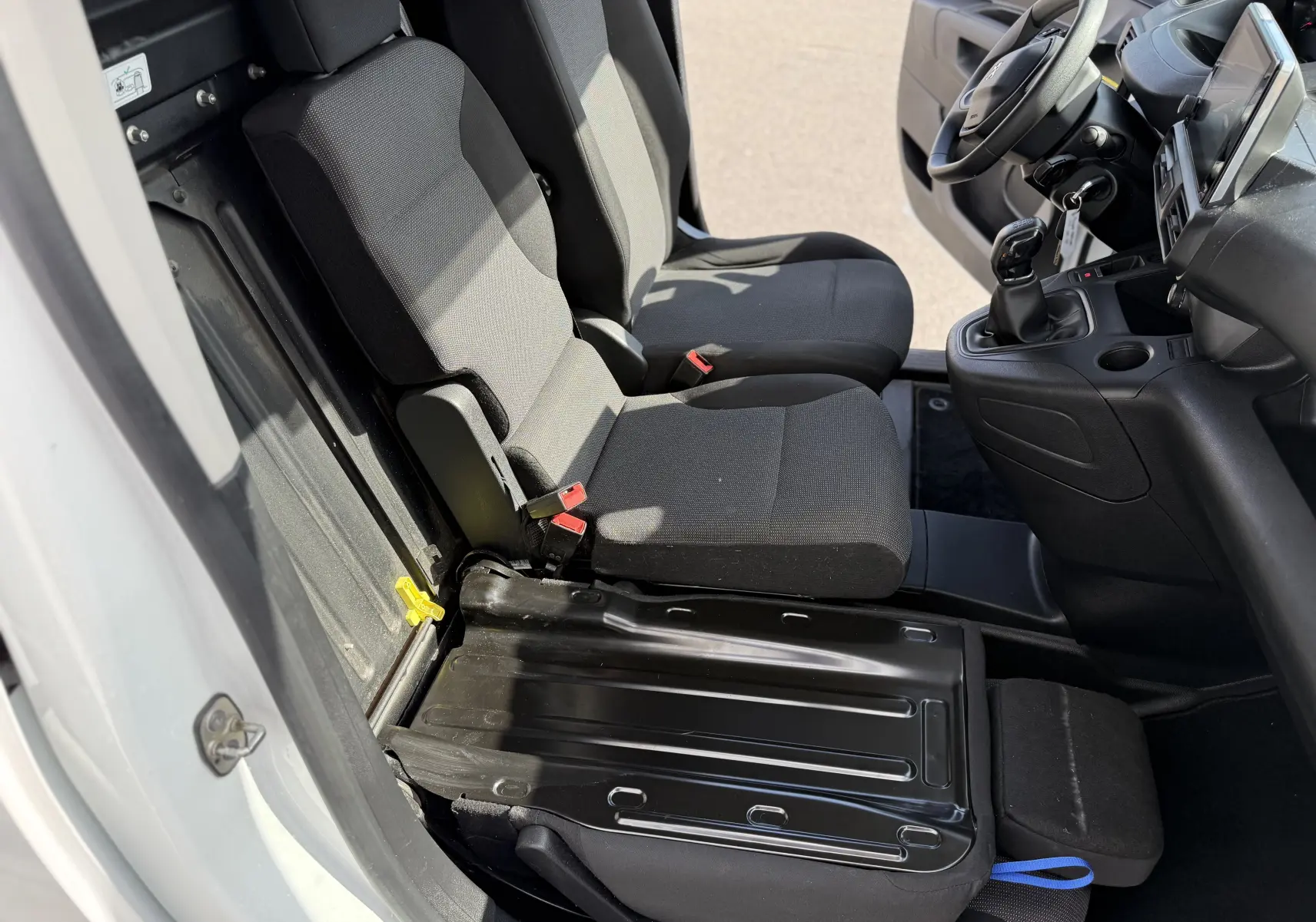 Vue intérieure côté gauche du Peugeot Partner blanc 2021, montrant les sièges avant en tissu noir et la console centrale.