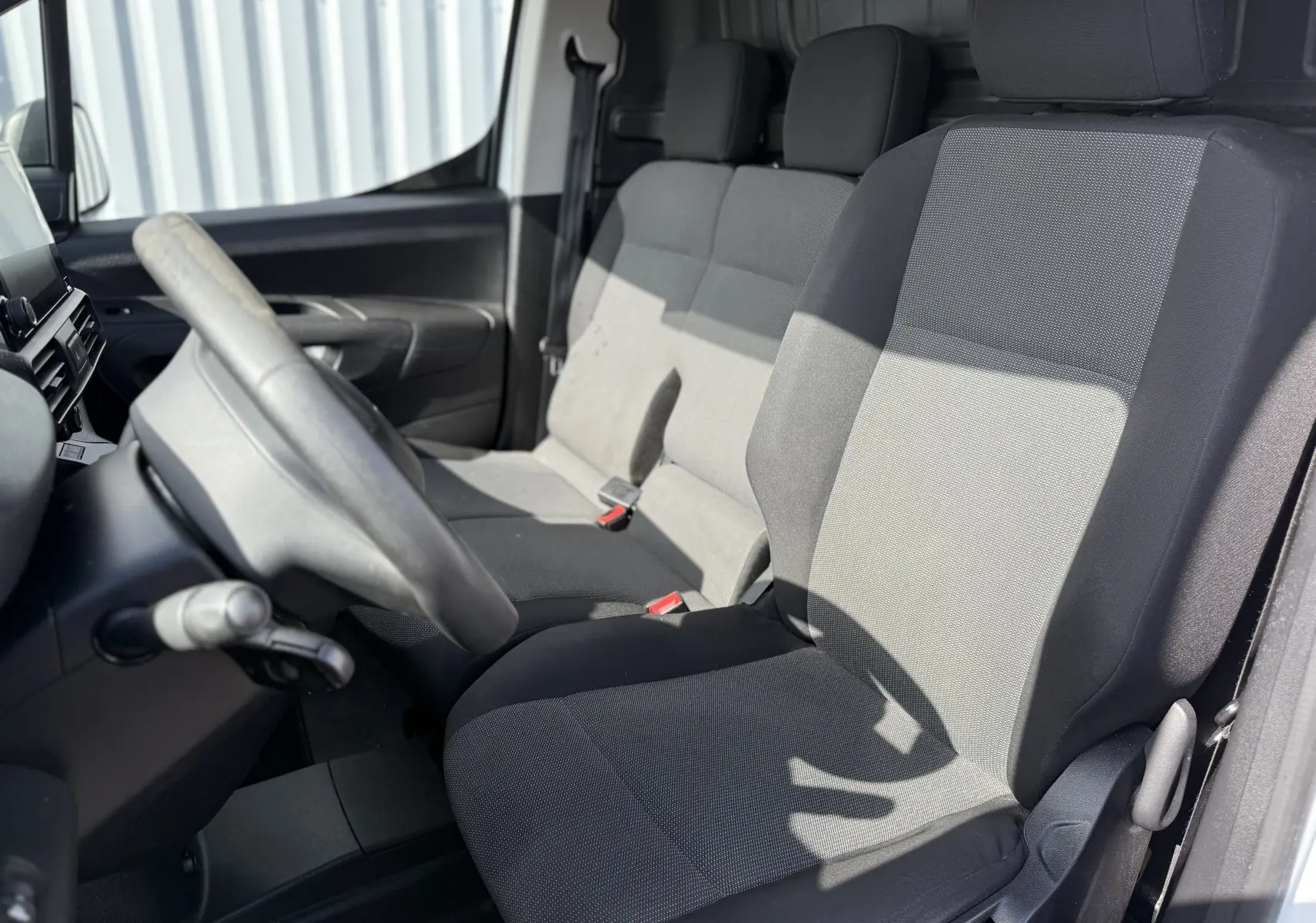Vue intérieure côté conducteur du Peugeot Partner 2021 blanc, montrant les sièges avant gris et noir en tissu.