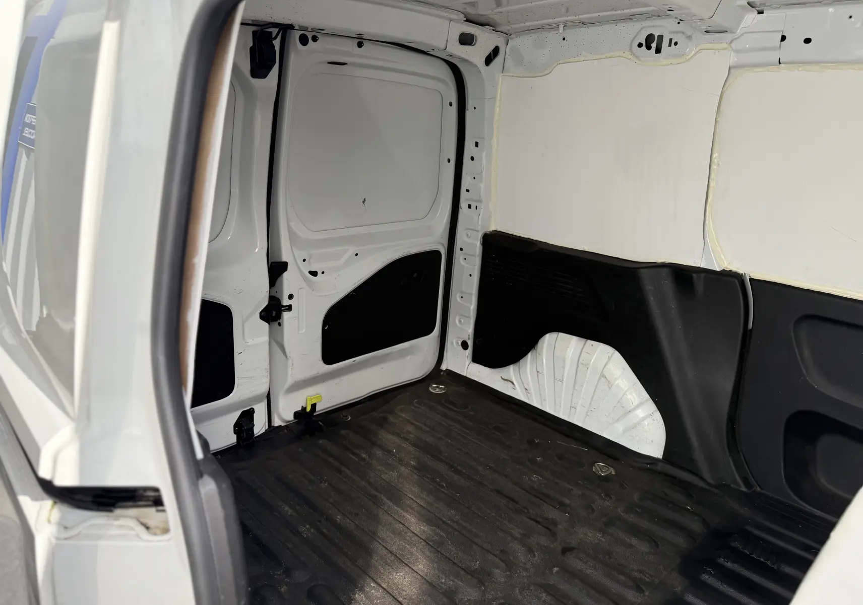 Intérieur arrière du Peugeot Partner blanc 2021, vue depuis la porte latérale ouverte, espace de chargement vide avec revêtement noir.