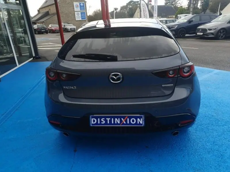 Vue arrière d'une Mazda3 2.5 e-SKYACTIV-G hybride 2024 en Platinum Quartz Métallisé avec feux arrière LED et lunette surteintée.