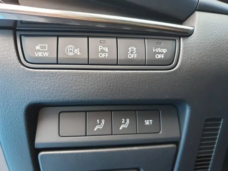 Boutons de commandes noirs sur tableau de bord gris foncé de la Mazda3 2024, avec réglages sièges et aides à la conduite.