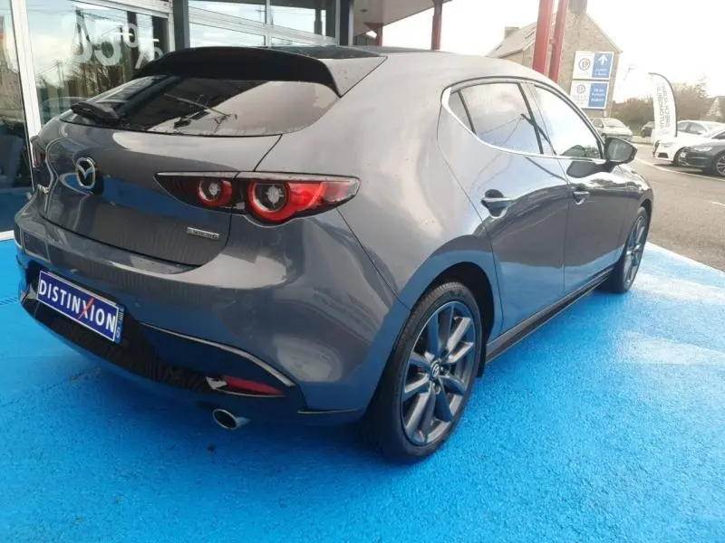 Vue 3/4 arrière droite d'une Mazda3 2024 Platinum Quartz Métallisé avec jantes alu et feux arrière LED distinctifs.