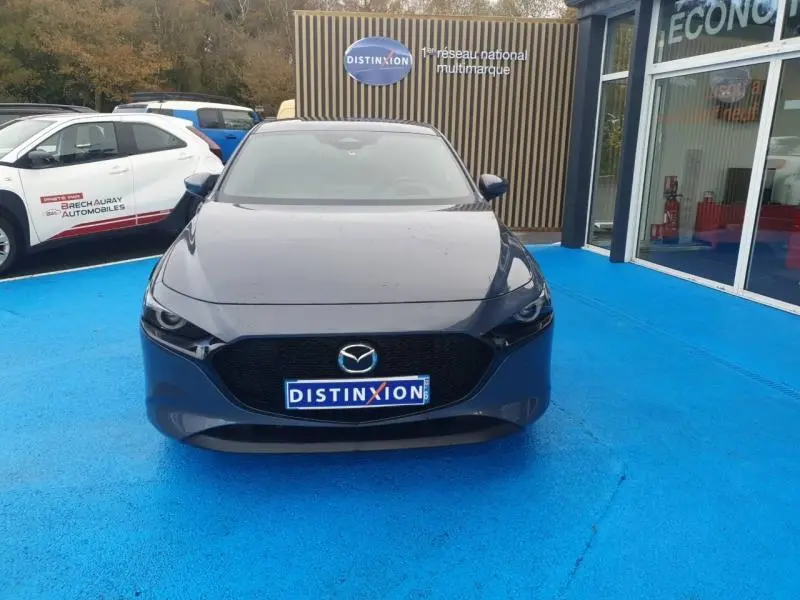 Vue avant d'une Mazda3 2024 bleu foncé avec calandre noire et logo Mazda sur parking bleu
