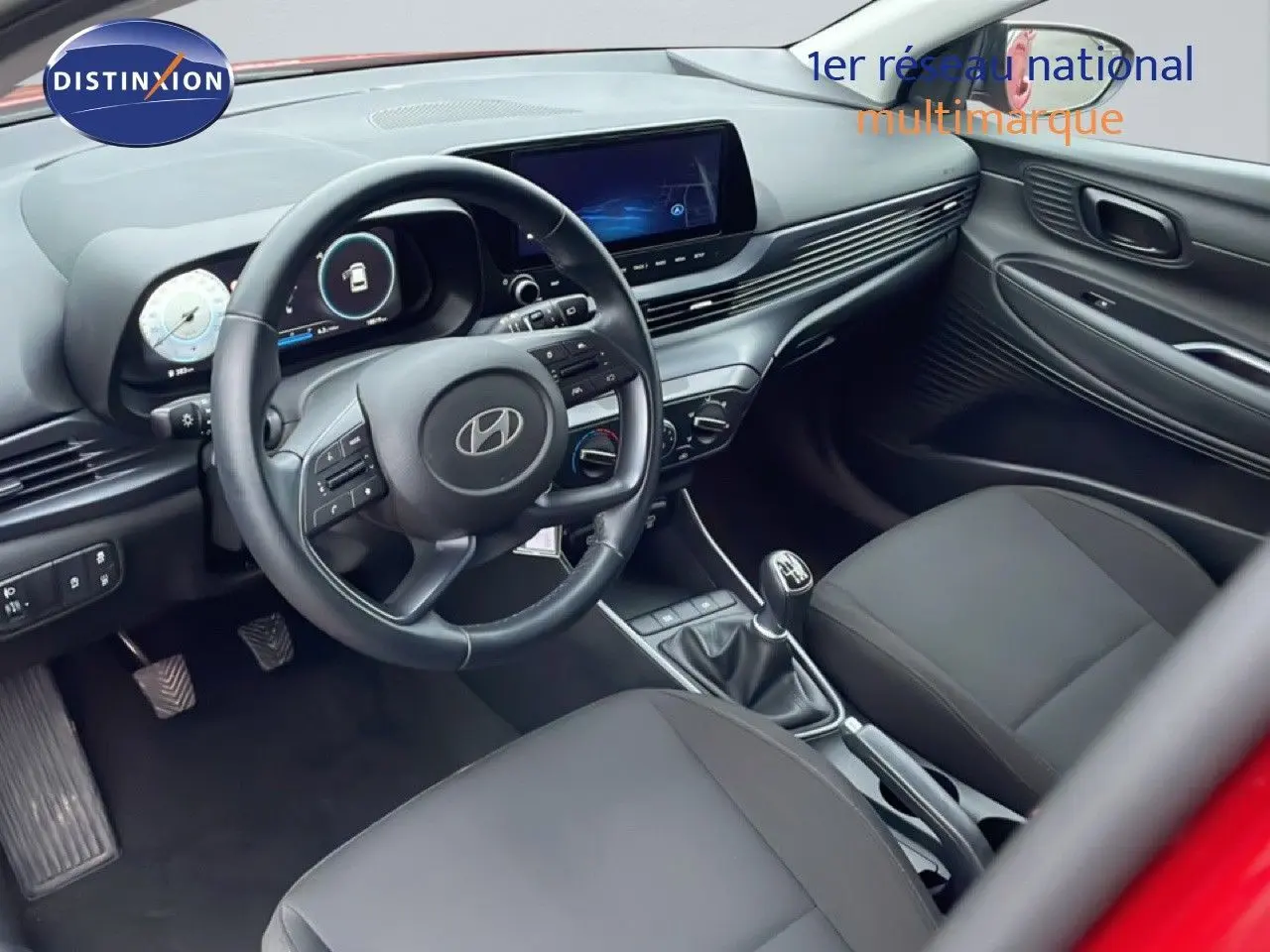 Intérieur noir de la Hyundai i20 2025, vue côté conducteur montrant volant cuir, tableau de bord digital et boîte manuelle.