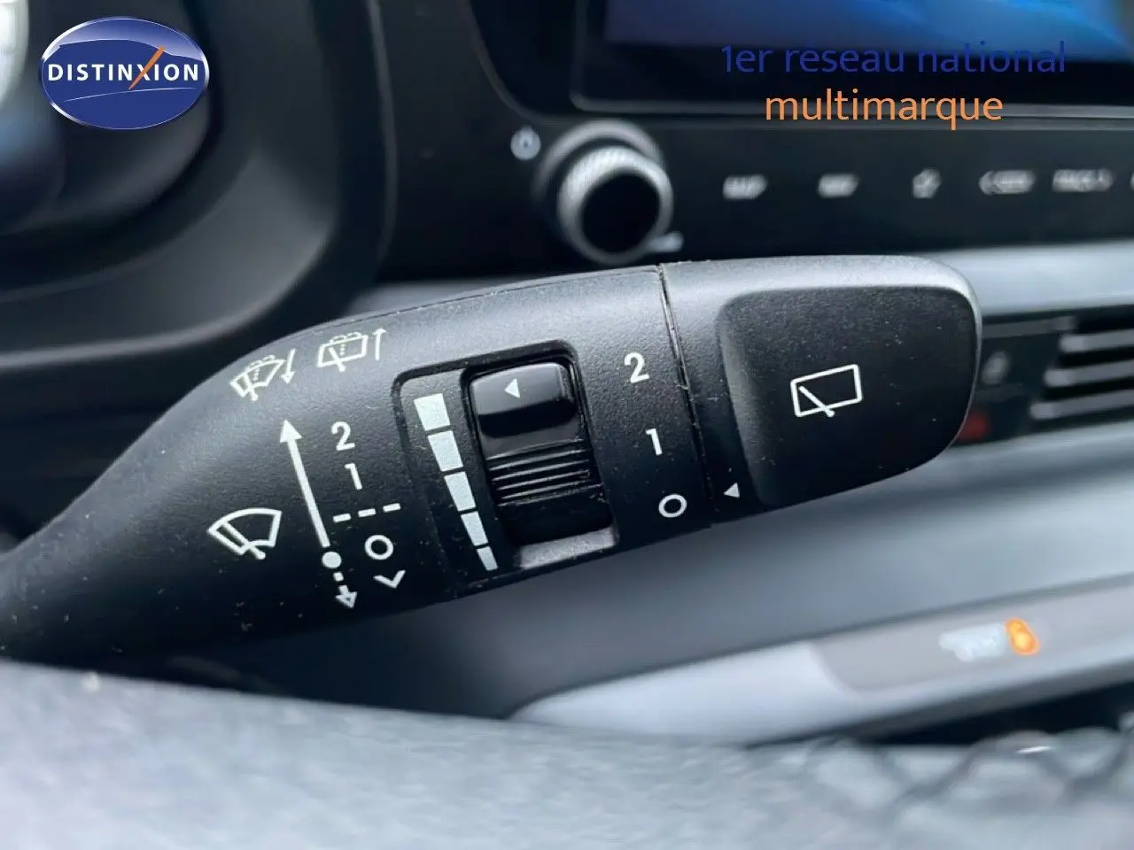 Gros plan sur la commande d'essuie-glace du volant d'une Hyundai i20 rouge Dragon Metal, intérieur noir visible en arrière-plan.