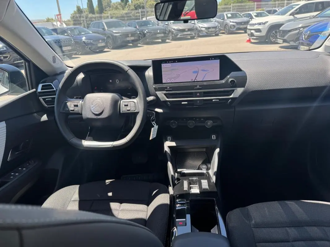 Vue intérieure avant du Citroën C4 hybride blanc 2025, avec volant cuir, écran tactile et console centrale moderne.