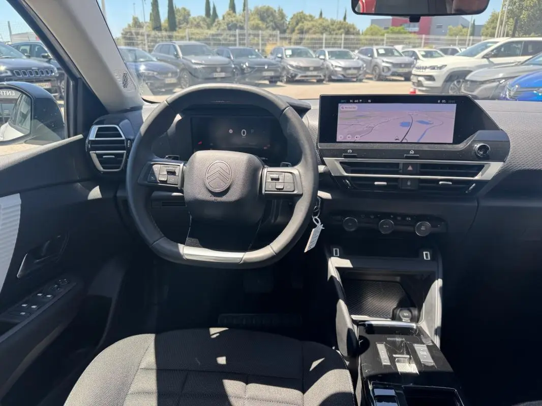 Vue intérieure avant du poste de conduite de la Citroën C4 blanche, avec volant cuir et écran tactile central affichant la navigation.