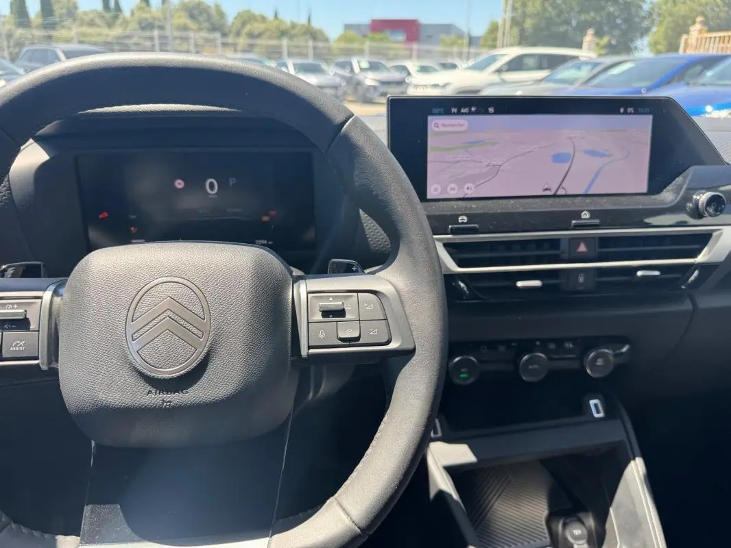 Vue intérieure centrée sur le volant cuir et l'écran tactile du tableau de bord du Citroën C4 blanc hybride 2025.