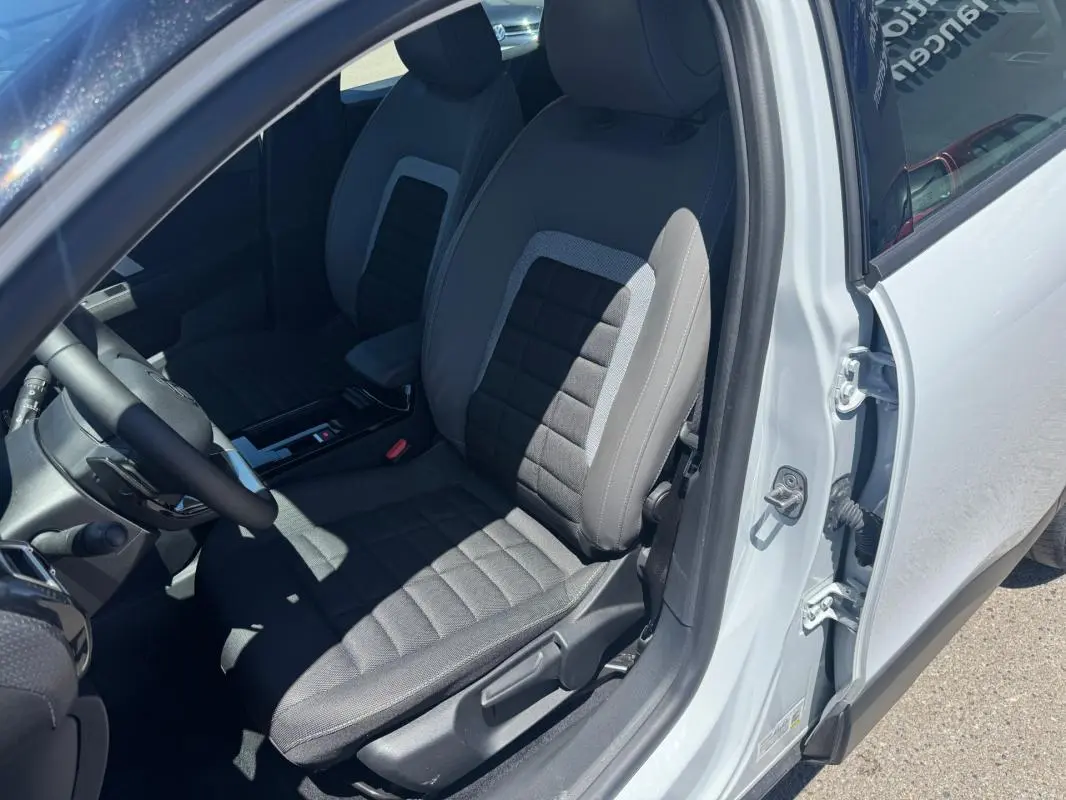 Vue intérieure côté conducteur de la Citroën C4 blanche 2025, montrant le siège avant en tissu gris et noir.